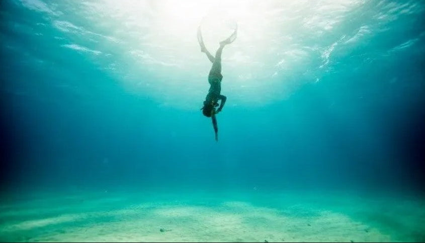 Person free diving underwater in clear blue water